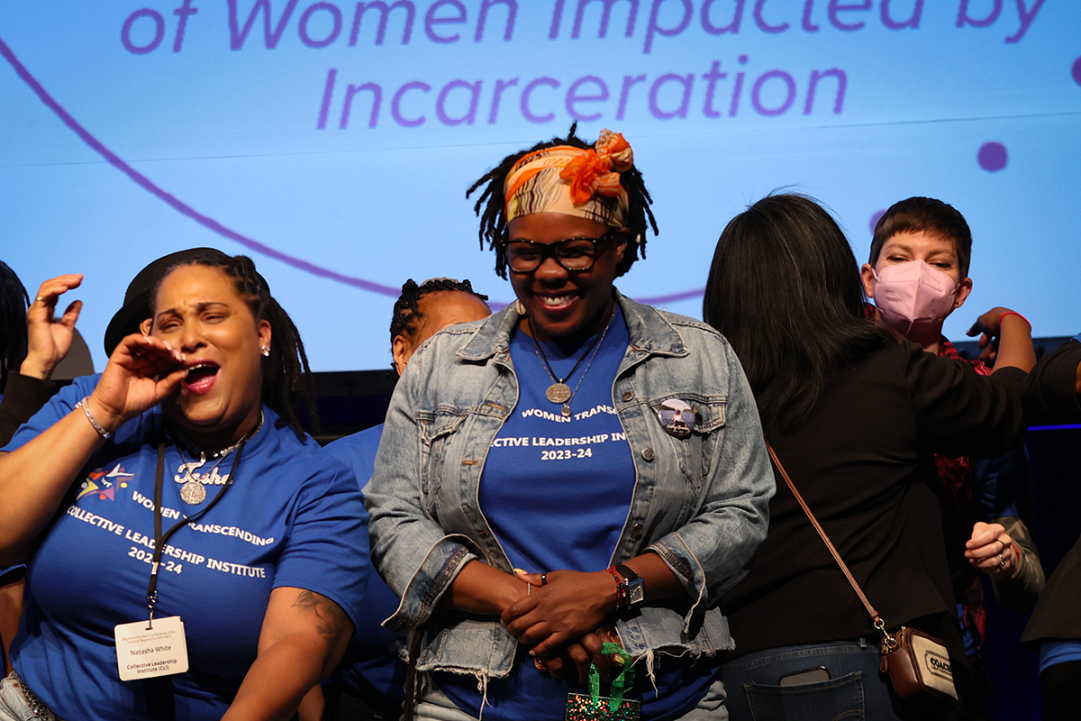 Women on stage in matching blue shirts cheering and hugging each other