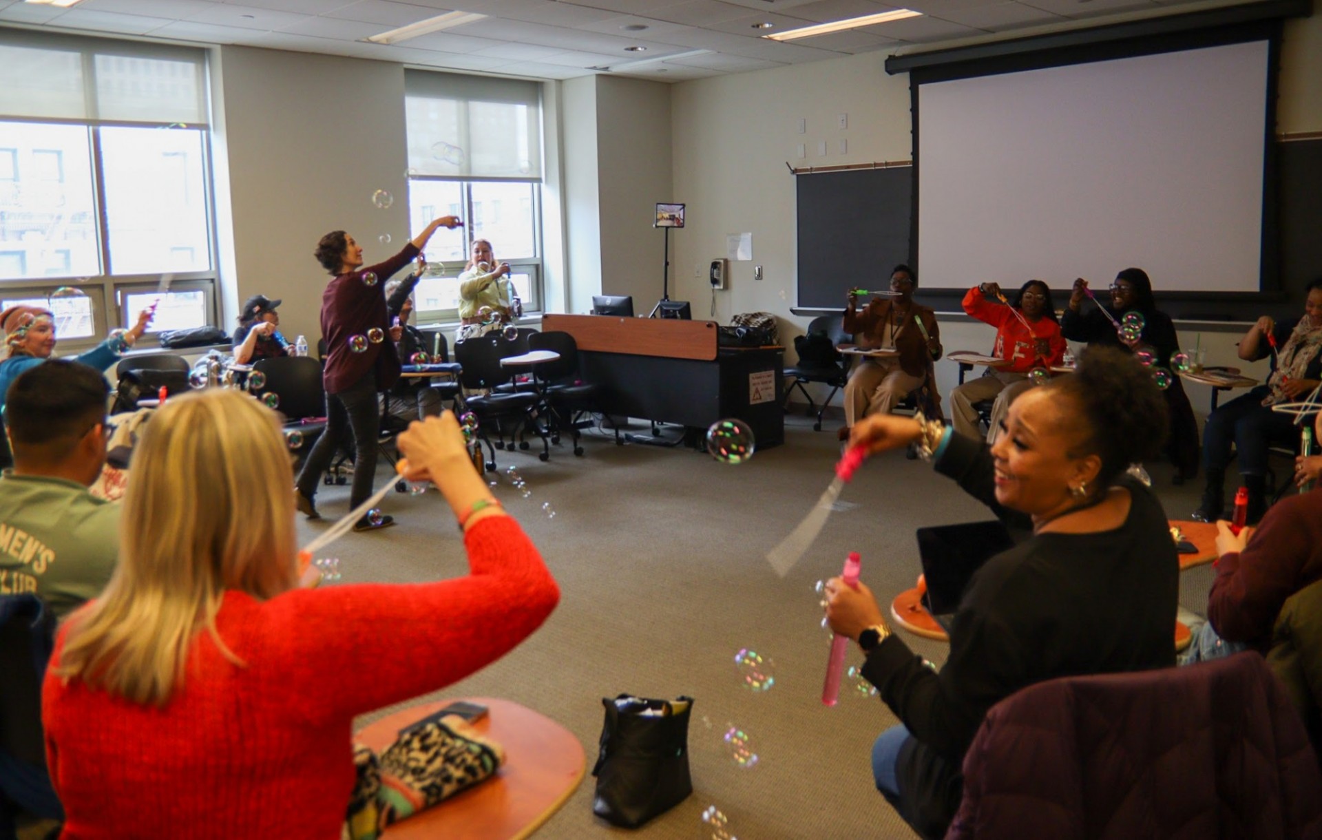 People in a classroom sitting in a circle and blowing bubbles as a part of a workshop exercise